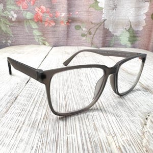May include: Gray rectangular eyeglasses with clear lenses. The glasses have a matte finish and a subtle gradient on the frames. The text "CHINA/CHINE MS0425 VLER2311 GRY" is printed on the temple.