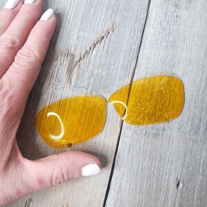May include: Two yellow-tinted replacement lenses for sunglasses. The lenses are curved and have a slight tint.