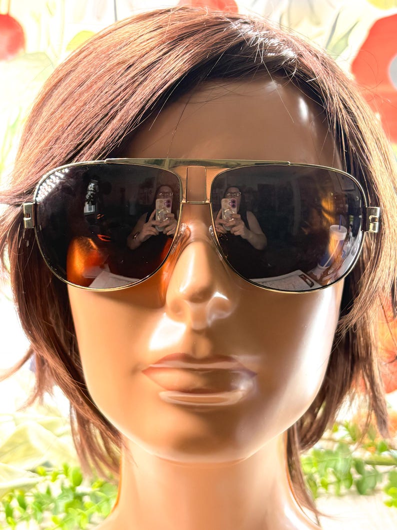 Op de afbeelding: Aviator zonnebril met een goudkleurig metalen montuur, een dubbele brug en donkere, reflecterende glazen. De zonnebril heeft een klassieke druppelvorm met dunne pootjes en ge&iuml;ntegreerde neuspads voor een gestructureerde uitstraling.