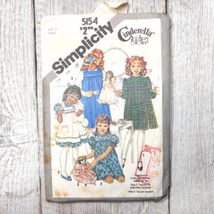 Pode incluir: Padrão de costura Simplicity vintage para vestido infantil, tamanho 3. O envelope do padrão apresenta ilustrações de meninas em vários vestidos, incluindo um macacão azul e um vestido xadrez verde. O logotipo da Cinderela é visível.
