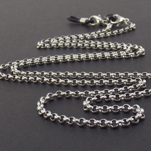 May include: A silver chain with a black cord and two silver clasps. The chain is made of small, round links.