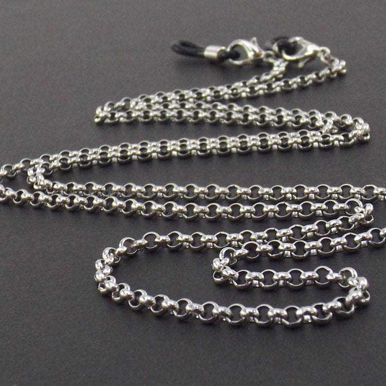 May include: A silver chain with a black cord and two silver clasps. The chain is made of small, round links.