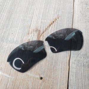 Op de afbeelding: Twee zwarte vervangende glazen voor zonnebrillen. De glazen zijn gebogen en hebben een reflecterende coating.