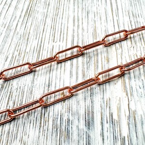 May include: Close-up of two copper-colored chain strands. The chains have a rectangular link design. The chains are displayed on a light-colored, textured surface. The chains are likely used for jewelry making or as decorative elements.
