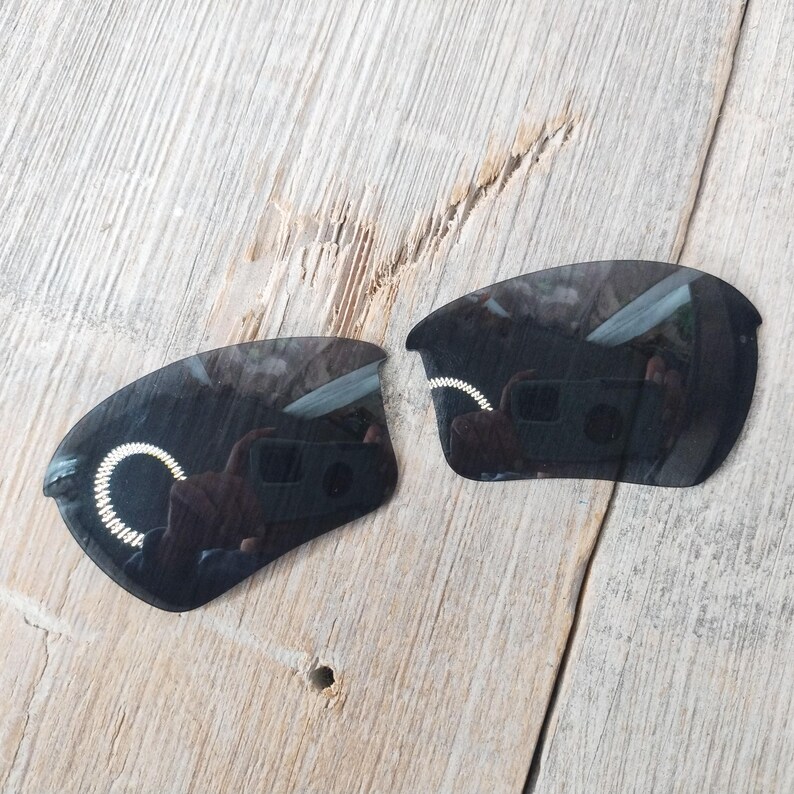 Op de afbeelding: Twee zwarte vervangende glazen voor zonnebrillen. De glazen zijn gebogen en hebben een donkere tint.