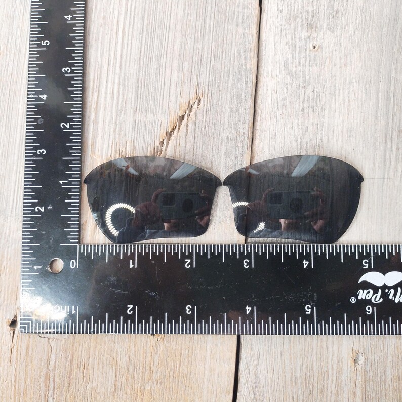 Op de afbeelding: Een paar zwarte vervangende glazen voor zonnebrillen. De glazen worden gemeten met een liniaal en zijn ongeveer 5 cm breed.