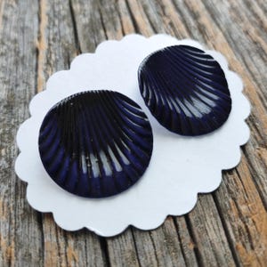 May include: A pair of dark blue shell-shaped earrings. The earrings are made of glass and have a textured surface.