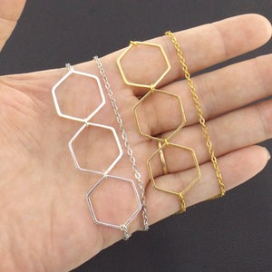 Op de afbeelding: Twee kettingen met zeshoekige hangerbedels. De ene ketting heeft zilveren bedels en een zilveren ketting, de andere heeft gouden bedels en een gouden ketting.