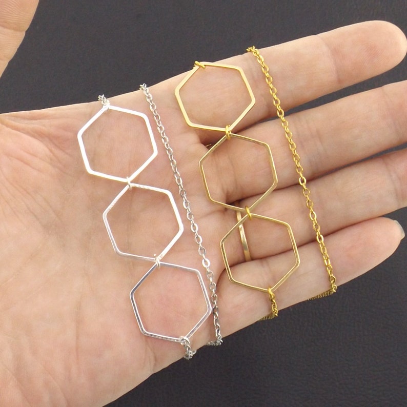 Op de afbeelding: Twee kettingen met zeshoekige hangerbedels. De ene ketting heeft zilveren bedels en een zilveren ketting, de andere heeft gouden bedels en een gouden ketting.