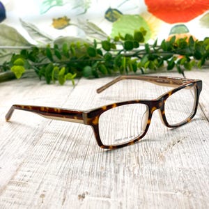 May include: A pair of eyeglasses with a tortoiseshell pattern frame. The rectangular frames have clear demo lenses and the text "DEMO LENS ONLY" is visible. The temples are a gradient of brown and tan. The glasses rest on a light-colored wooden surface.
