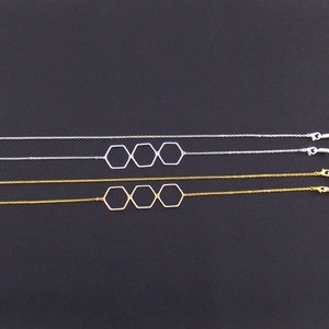 Op de afbeelding: Twee delicate kettingen met een drie-hexagon hanger ontwerp. E&eacute;n ketting is zilver en de andere is goud.