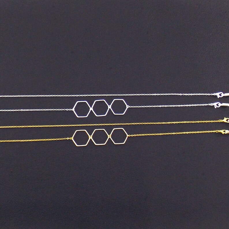 Op de afbeelding: Twee delicate kettingen met een drie-hexagon hanger ontwerp. E&eacute;n ketting is zilver en de andere is goud.