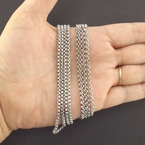 May include: Two silver chains, one thicker than the other, are laid out on a hand. The chains are made of small, linked circles.