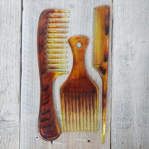May include: Three combs made of brown plastic with yellow teeth. The combs are on a light wood background.