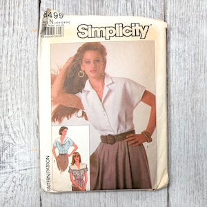 May include: Vintage Simplicity sewing pattern, size N (10+12+14), featuring a woman wearing a collared shirt and skirt. The pattern includes multiple views of the shirt. The package is slightly worn.