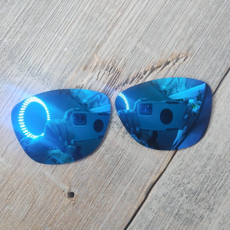 May include: Two blue mirrored replacement lenses for sunglasses. The lenses are curved and have a reflective blue coating.