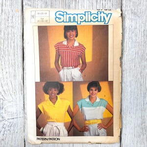 May include: Vintage Simplicity sewing pattern featuring three different blouse designs. The blouses are shown in red and white stripes, yellow, and blue and white color blocks. The pattern includes sizes 10, 12, and 14.