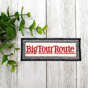 May include: A white fabric patch with black trim and the text "Big Four Route" in red embroidery.