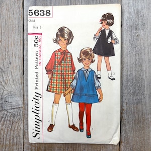 Könnte beinhalten: Vintage Simplicity Schnittmuster für ein Kinderkleid in Größe 5. Das Muster zeigt Illustrationen von drei verschiedenen Kleiderdesigns, darunter ein rot kariertes Kleid, ein blaues Kleid und ein schwarzes Kleid. Der Preis beträgt 50¢ in Kanada.