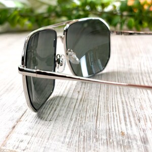 Pode incluir: &Oacute;culos de sol com arma&ccedil;&atilde;o prateada e lentes escuras. Os &oacute;culos de sol t&ecirc;m um formato aviador cl&aacute;ssico com ponte dupla e arma&ccedil;&atilde;o de metal fina. As lentes s&atilde;o de cor cinza escuro e a arma&ccedil;&atilde;o tem um acabamento brilhante.