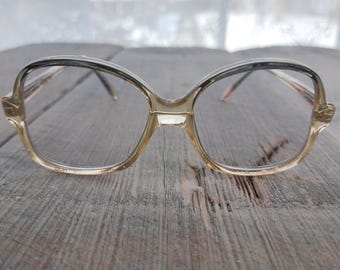 May include: A pair of vintage eyeglasses with a clear, light brown frame and square lenses. The frame has a subtle, dark brown accent along the top edge.