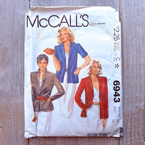 Può includere: Busta di cartamodello McCall's vintage con illustrazioni di donne in blazer. La busta è bianca con il logo McCall's e il numero del modello 6943. Le illustrazioni raffigurano un blazer marrone, blu e rosso.