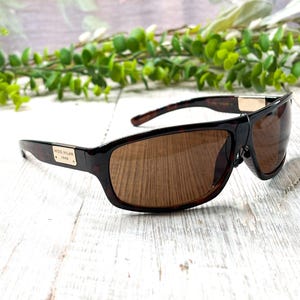 May include: Brown sunglasses with a tortoiseshell pattern on the frames and brown lenses. The sunglasses have a rectangular shape and a gold-colored accent on the temples. The text "MIDO MILAN 1945" is printed on the left arm.