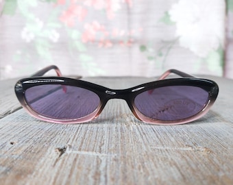 May include: Black sunglasses with pink frames and purple lenses. The lenses have "100 UV" printed on them.