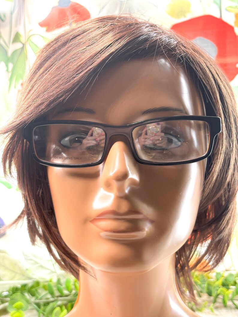 Pode incluir: Uma cabe&ccedil;a de manequim usando &oacute;culos retangulares pretos. Os &oacute;culos t&ecirc;m arma&ccedil;&atilde;o escura e lentes transparentes. O texto "DEMO LENS ONLY" &eacute; vis&iacute;vel nas lentes. O manequim tem cabelo castanho e tez bronzeada.