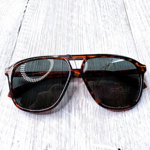 May include: Tortoiseshell aviator sunglasses with dark lenses. The sunglasses have a classic design with a double bridge and a sturdy frame. The lenses offer UV 400 protection.