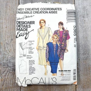 Op de afbeelding: Een vintage McCall's naaipatroon met ontwerpen van Dalmer Pletsch. Het pakket toont illustraties van dameskleding, waaronder jurken en een pak. De tekst bevat "Designer Details Made Easy" en maat 22.