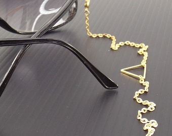 May include: A gold chain with a triangle charm attached to black eyeglasses. The chain is designed to keep the glasses from falling off.