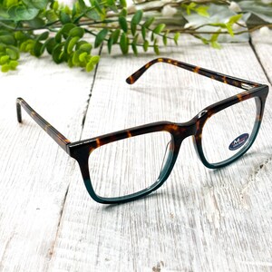 May include: Rectangular eyeglasses with a tortoiseshell pattern on the frames, fading to teal at the bottom. The glasses are set against a white wooden background. The lenses are clear.