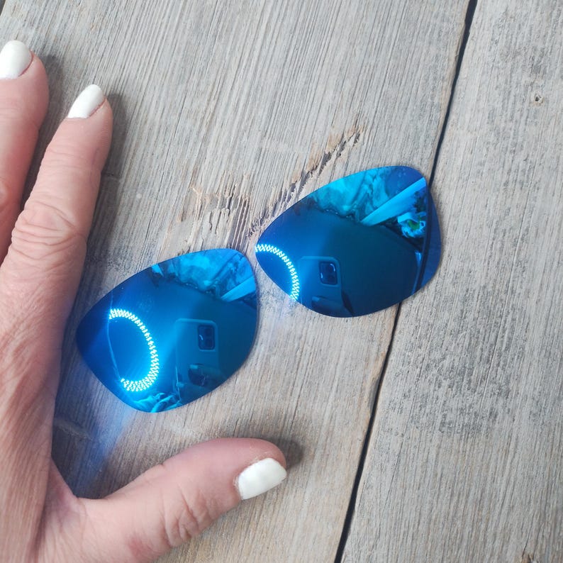 May include: A pair of blue mirrored sunglasses with a reflective blue coating. The sunglasses are on a wooden surface.