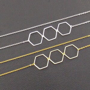 Op de afbeelding: Twee delicate kettingen met drie verbonden zeshoekige hangers. De bovenste ketting heeft zilverkleurige zeshoeken en een zilveren ketting. De onderste ketting heeft goudkleurige zeshoeken en een gouden ketting.