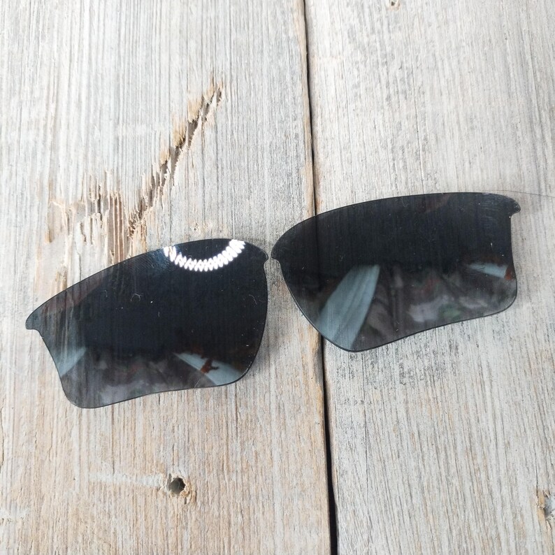 Op de afbeelding: Een paar zwarte vervangende glazen voor zonnebrillen. De glazen zijn gebogen en hebben een donkere tint.
