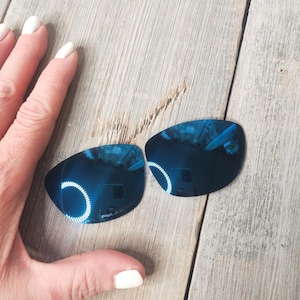 May include: Two blue mirrored replacement lenses for sunglasses. The lenses are curved and have a reflective blue coating.