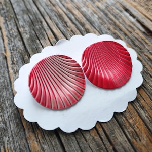 May include: A pair of red and white shell-shaped earrings. The earrings are round and have a textured surface.