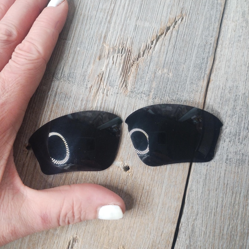 May include: A pair of black replacement lenses for sunglasses. The lenses have a silver ring around the edge.