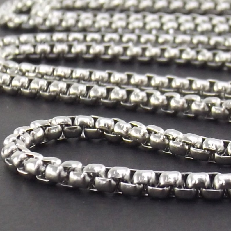 May include: A silver chain necklace with a box chain design. The chain is made of small, square-shaped links.