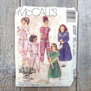 Peut inclure: Patron de couture McCall's vintage pour vêtements d'enfants. Le patron présente des illustrations de différentes tenues, dont des robes et des pyjamas. Le texte sur le patron indique "Fashion Basics for Kids" et comprend des informations sur les tailles.