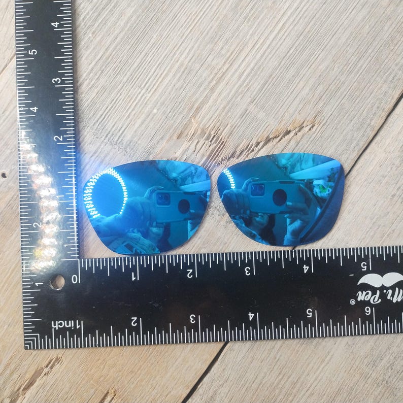 May include: Two blue mirrored replacement lenses for sunglasses. The lenses are curved and have a reflective blue coating.