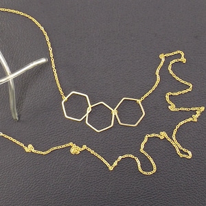 Op de afbeelding: Een gouden ketting met drie verbonden zeshoekige hangercharms.
