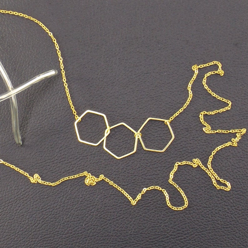 Op de afbeelding: Een gouden ketting met drie verbonden zeshoekige hangercharms.