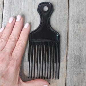 May include: A black plastic comb with a wide handle and a row of teeth. The comb is about 6 inches long.