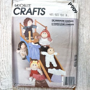 May include: A McCall's Crafts sewing pattern envelope, P909, for a 45.5cm soft-sculptured doll wardrobe. The cover features five dolls in various outfits, including a blue dress and white pyjamas, posed on a wooden structure. Text includes "THE WARDROBE COMPLETE FOR YOUR 45.5cm SOFT-SCULPTURED DOLL."