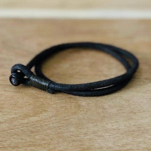 Può includere: Un braccialetto in corda nera con una piccola chiusura in metallo nero.