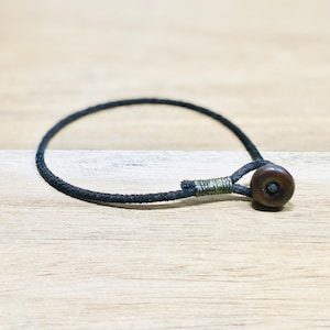 May include: A simple black cord bracelet with a dark brown wooden bead.