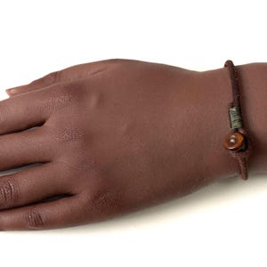 May include: A brown leather bracelet with a wooden bead and a green and brown cord accent.