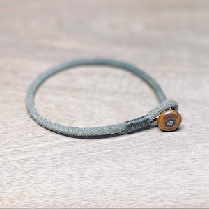 Puede incluir: Un brazalete de cuero gris con una cuenta de madera marrón.